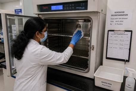 Lab technician decontaminating the interior of a CO2 incubator with 70% ethanol wipes in a Karnataka cell culture facility during scheduled maintenance